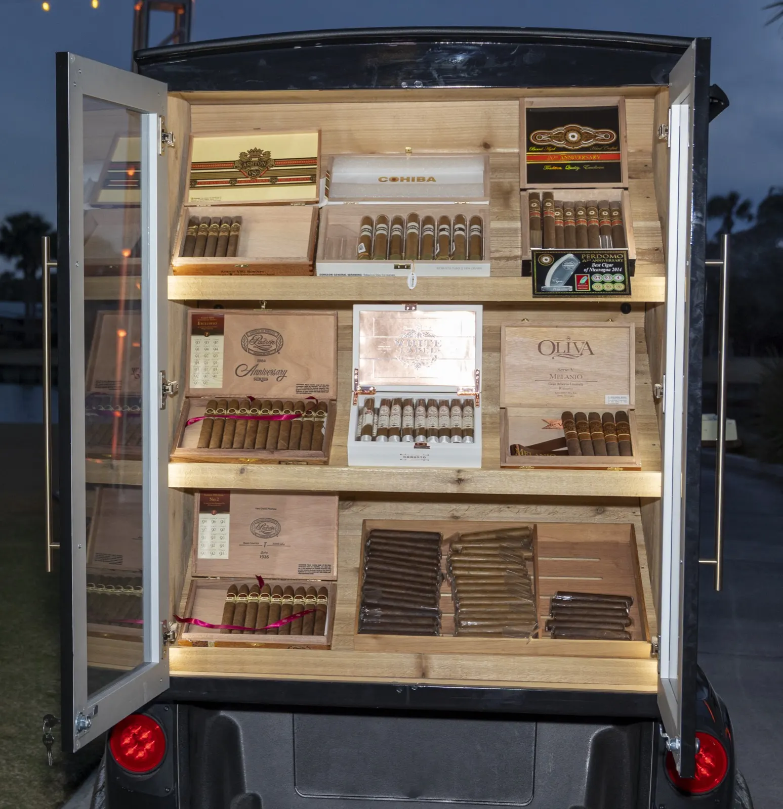 Glass humidor doors open on the cigar golf cart showing shelves of premium cigars