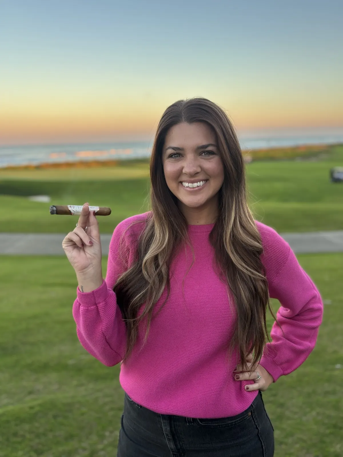 Hannah holding a cigar at golden hour on the course
